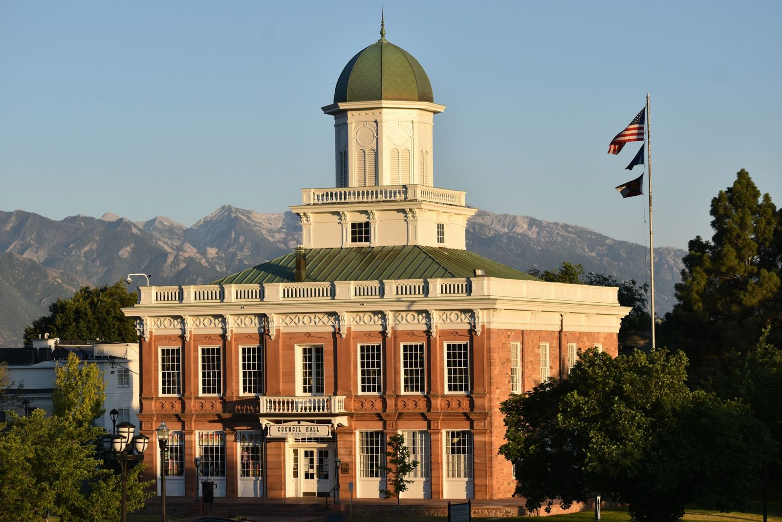 A historic civic building with a flag in front of mountains