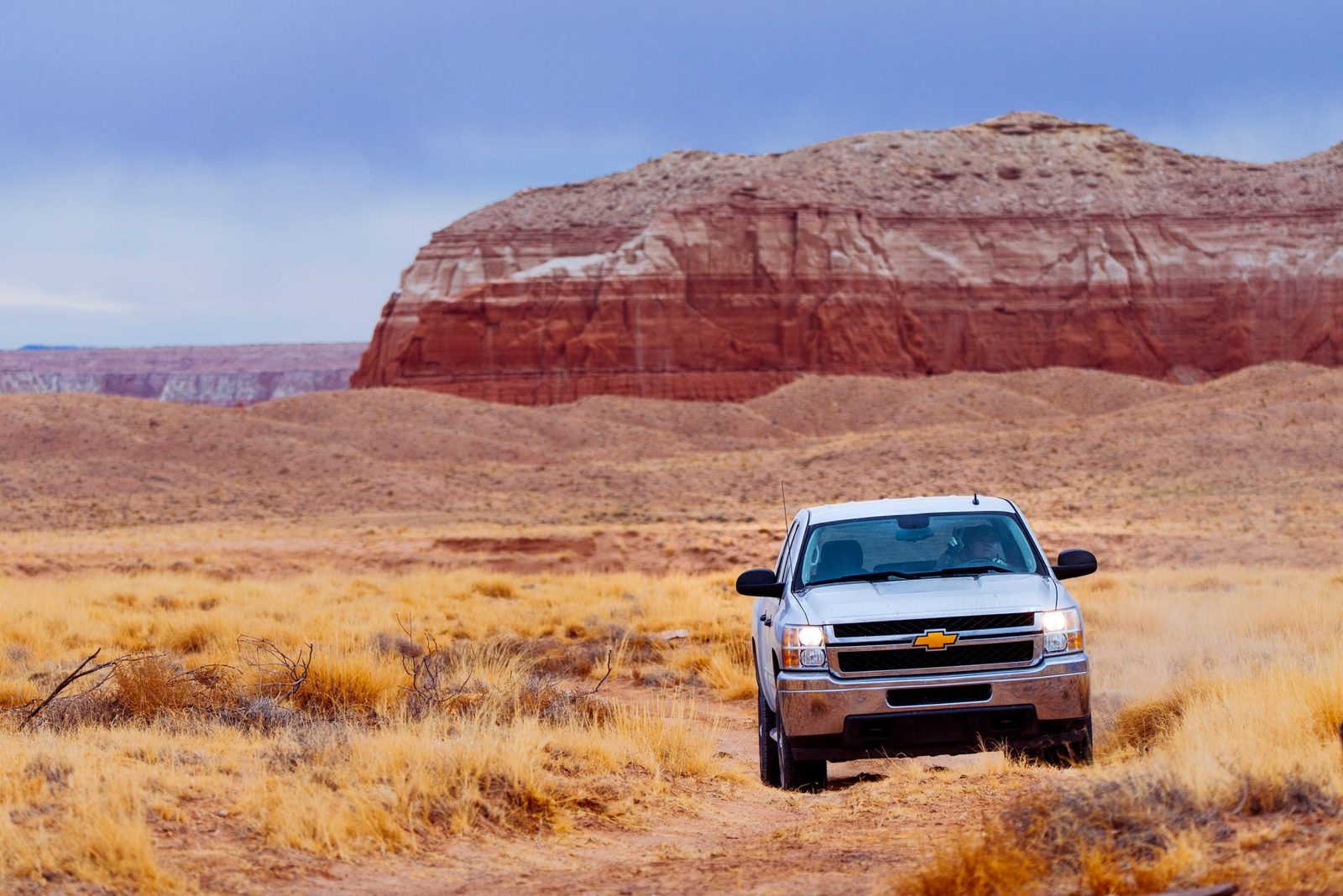 A pickup truck on open desert ground below a red mesa