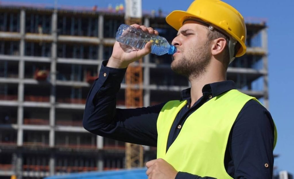 Construction workers pausing at a shaded water point during a high heat shift