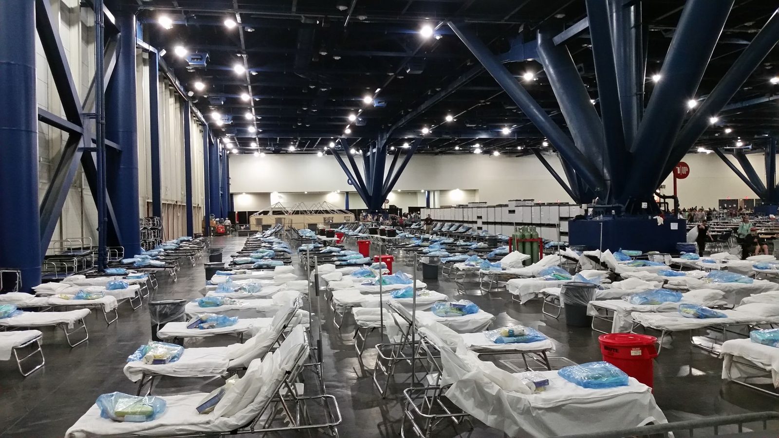 Rows of cots set up inside a large hall used as an emergency shelter