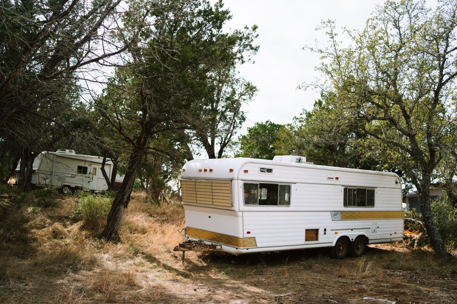 Travel trailers parked under trees at a work camp