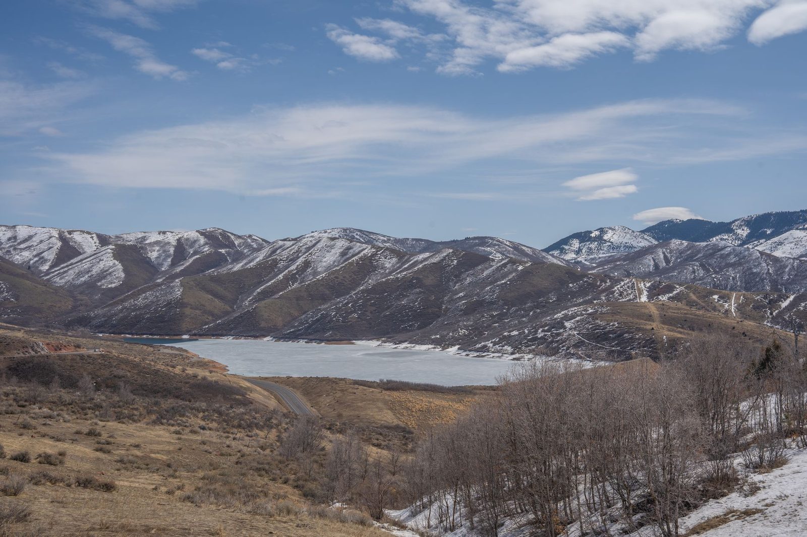 Snow-dusted brown mountains above a reservoir under a clear sky