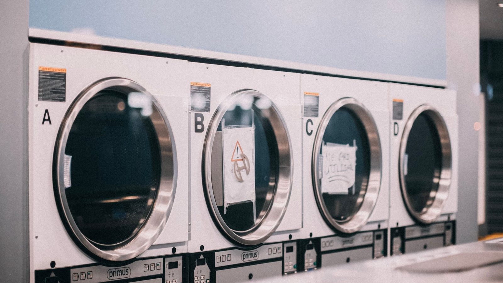 A row of front-load washers labeled A through D in a shared laundry room