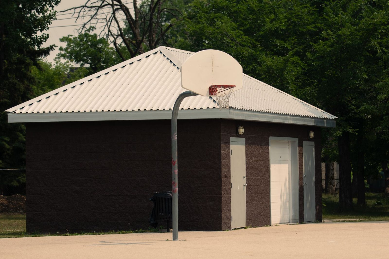 A small park restroom building beside a basketball court