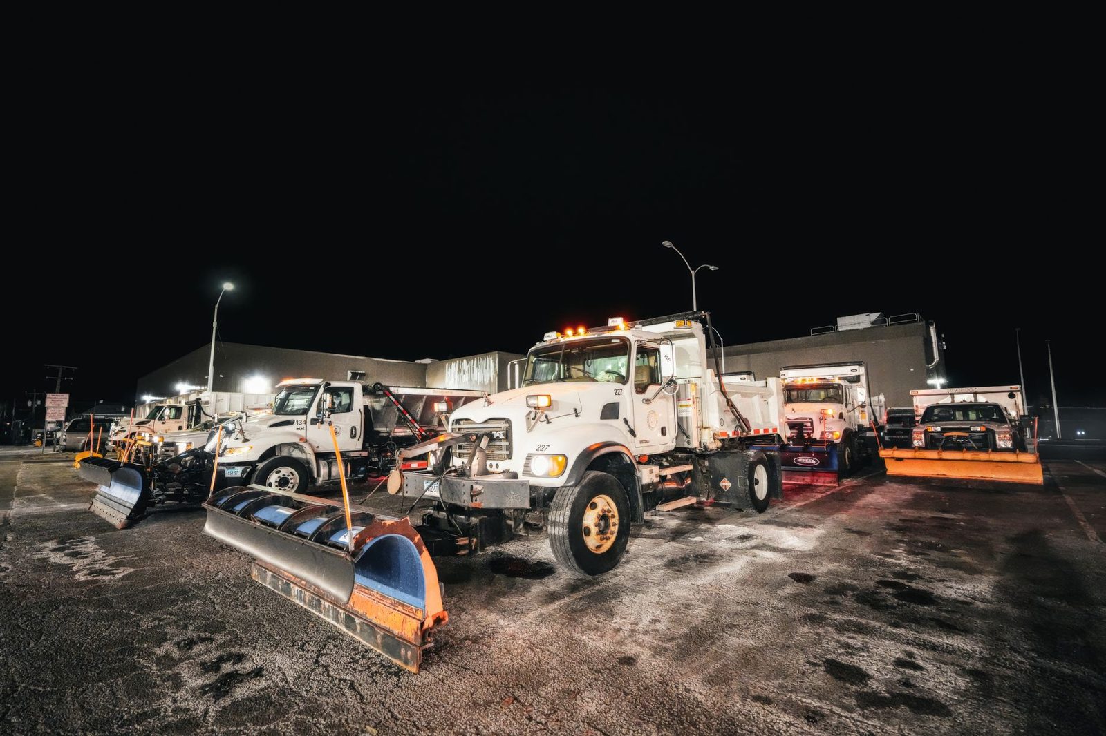 City plow trucks lined up in a yard at night