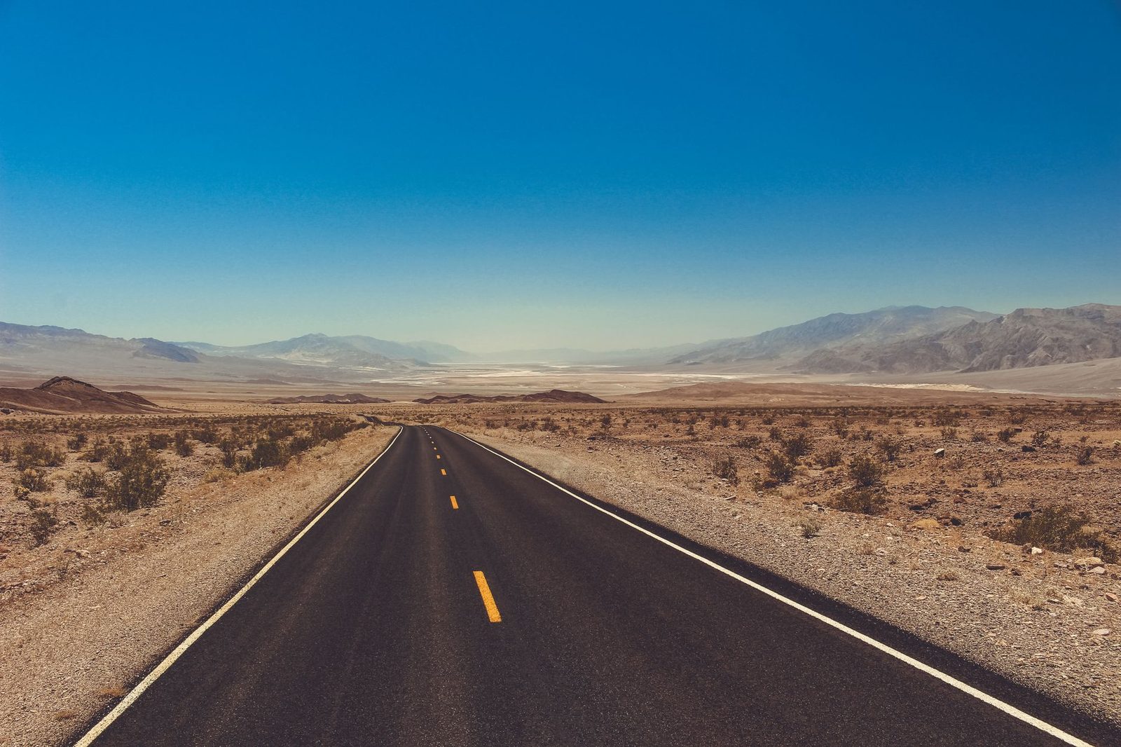 A straight desert highway running across a hot, dry valley floor