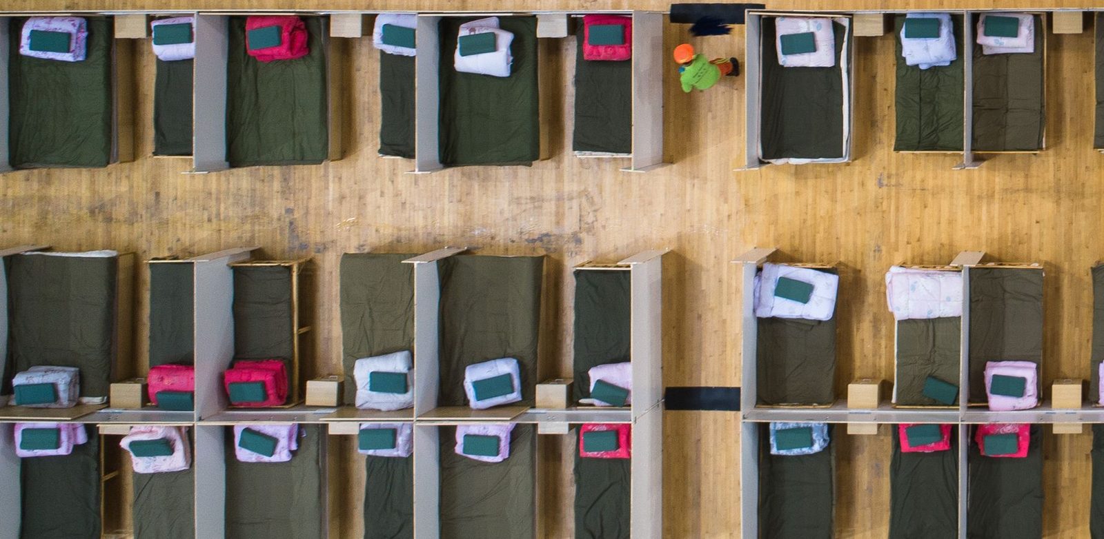 Rows of cots laid out on a gymnasium floor set up as an emergency shelter