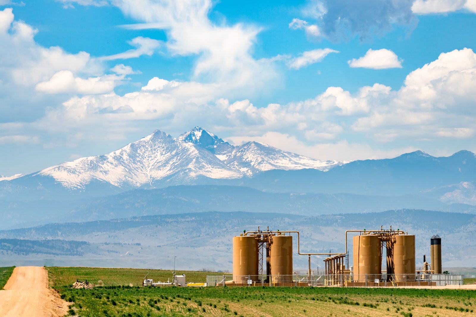 Snow-capped Front Range peaks above farm fields and storage tanks on the plains
