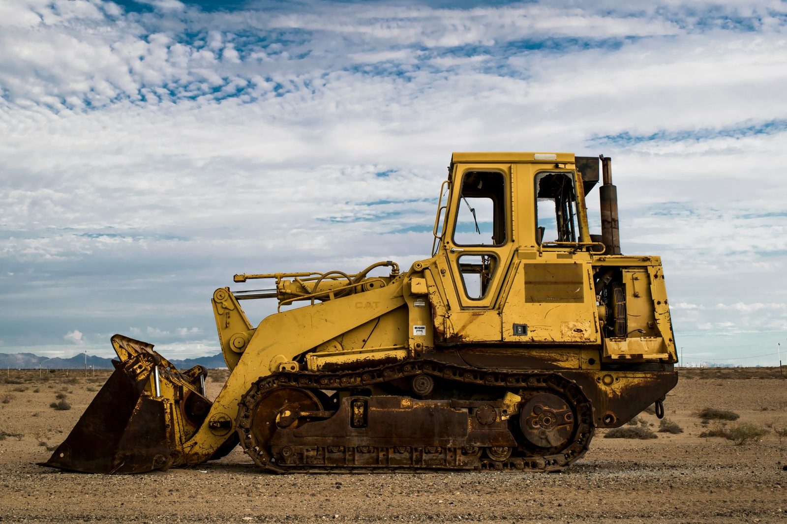 A track loader parked on a flat desert work site with low mountains on the horizon