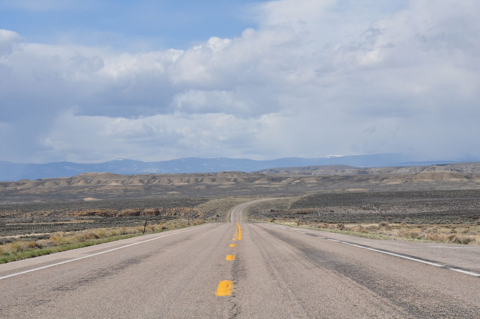 A long two-lane highway running across an open high desert basin toward distant mountains