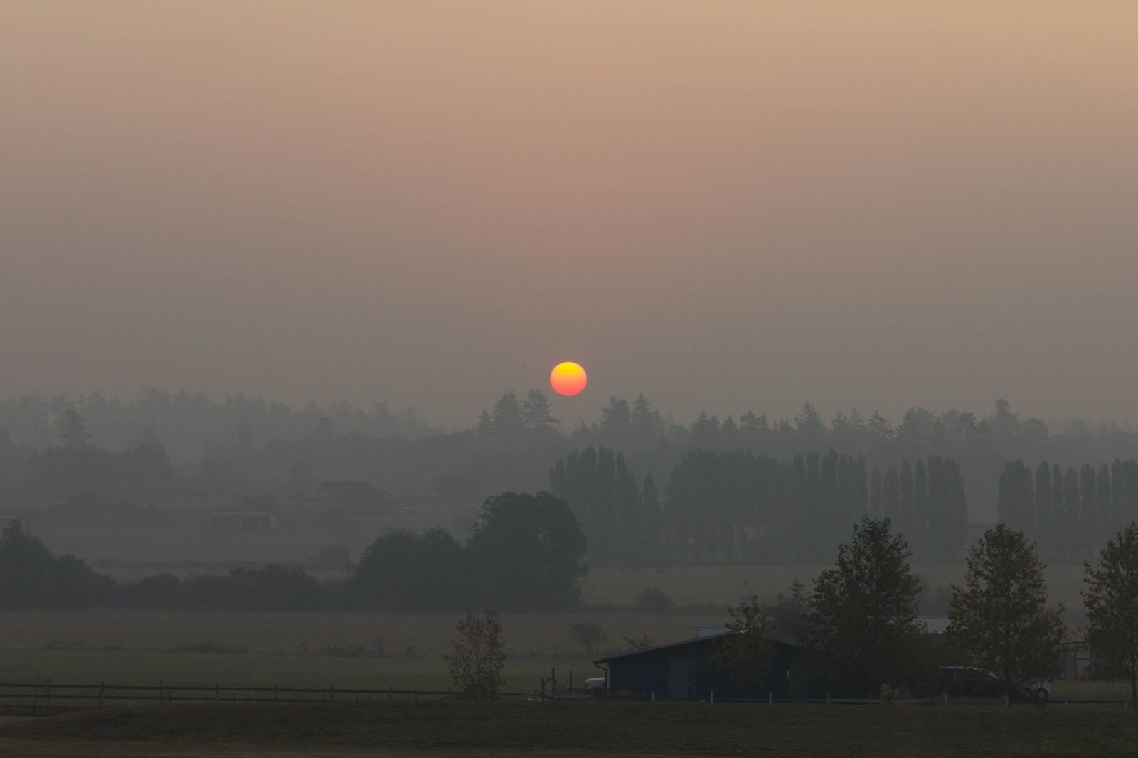 The sun glowing orange through heavy smoke haze over a valley