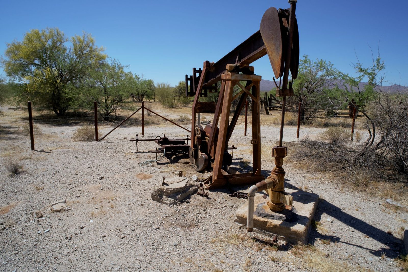A rusted pumpjack on dry, open desert ground